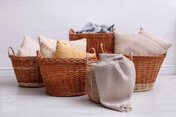 Many different wicker baskets with pillows and blankets indoors