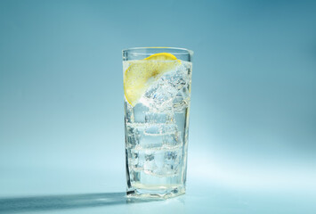 Soda water with lemon and ice cubes in glass on light blue background