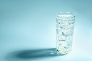 Soda water with ice cubes in glass on light blue background, space for text