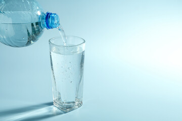 Pouring soda water from bottle into glass on light blue background, space for text