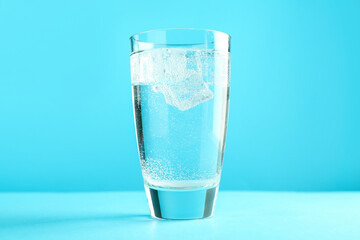 Soda water with ice cubes in glass on light blue background