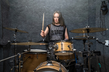 Female drummer playing drum kit in soundproof studio. Focused musician holding drumsticks,...