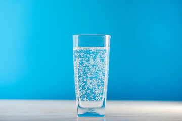 Refreshing soda water in glass on wooden table against light blue background, closeup