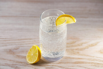 Refreshing soda water in glass and cut lemon on wooden table, closeup