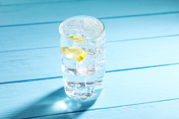 Refreshing soda water with ice cubes and slice of lemon in glass on light blue wooden table, closeup