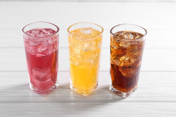 Soda water of different flavors with ice cubes in glasses on white wooden table