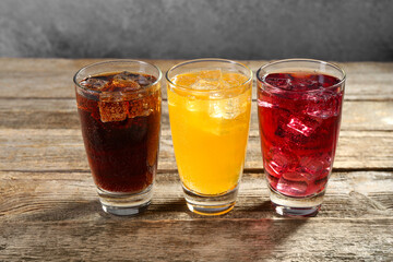 Soda water of different flavors with ice cubes in glasses on wooden table