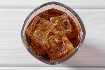 Sweet soda water with ice cubes in glass on white wooden table, top view