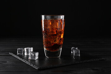 Sweet soda water in glass with ice cubes on black wooden table