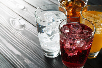 Refreshing soda water of different flavors with ice cubes in glasses on black wooden table, closeup. Space for text