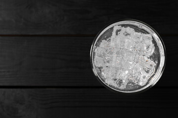 Refreshing soda water with ice cubes in glass on black wooden table, top view. Space for text