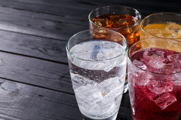 Refreshing soda water of different flavors with ice cubes in glasses on black wooden table, closeup. Space for text