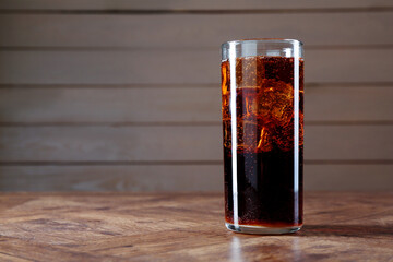 Sweet soda water with ice cubes in glass on wooden table, space for text