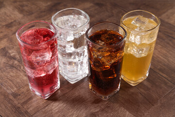 Refreshing soda water of different flavors with ice cubes in glasses on wooden table