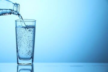 Pouring soda water from bottle into glass on light blue background, closeup. Space for text