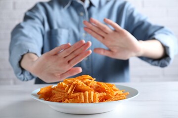 Woman refusing to eat chips at white table, selective focus. Food allergy concept