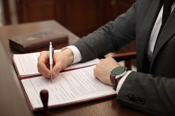 Notary signing document at wooden table in office, closeup