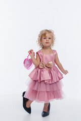 Young girl in a pink dress and high heels posing confidently against a plain background
