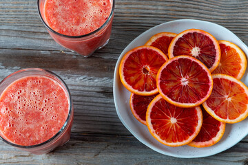Sliced Sicilian oranges with skin on a blue plate and two glasses of orange drink. Rustic wooden background. 