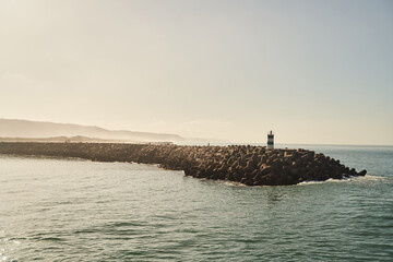 Fototapeta premium A picturesque lighthouse on the pier with a sunset over calm ocean waves creates a serene atmosphere