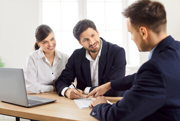 Happy family couple of clients is signing a contract or deal with agent, adviser, or consultant in the office. Important agreements in real estate, insurance, or financial matters.
