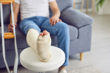 Close-up of handicapped man with leg in cast with crutch sitting on sofa at home in rehabilitation...