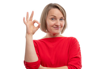 Fototapeta premium A smiling woman in a red shirt showing an okay hand gesture against a white background.