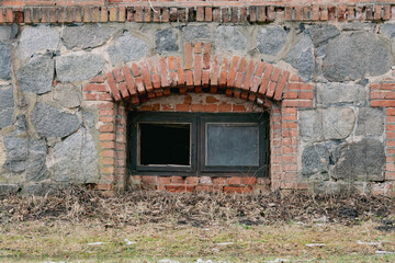Decaying Wall with Cracked Bricks and a Broken Glass Window. Mysterious Basement Window in an Aged...
