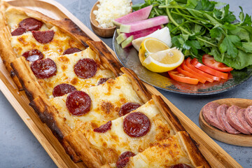 Turkish pide dish with slices of pepperoni and cheese. Turkish traditional pita. (pide with pepperoni) on wood service. Turkish name; Sucuklu pide.