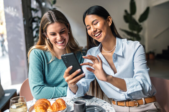 Two beautiful women friends talking while using smartphone in a coffee shop