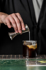 A bartender pours a creamy layer over a dark cocktail in a glass, highlighting the skillful preparation of a modern drink at a bar.
