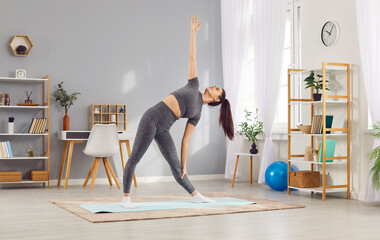 Sporty young woman doing sport morning exercise alone in living room, fit slim girl wearing...