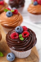 Tasty cupcakes with chocolate cream and berries on white marble table, closeup