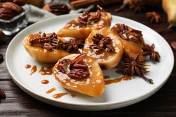 Delicious pears with caramel sauce, pecan nuts and anise stars on wooden table, closeup