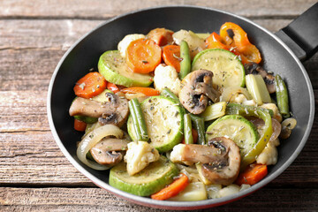 Different vegetables and mushrooms in frying pan on wooden table, closeup