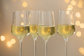 Tasty white wine in glasses against grey background with blurred lights, closeup. Bokeh effect
