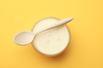 Tasty condensed milk in bowl and spoon on orange background, top view