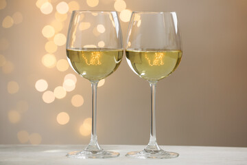 Tasty white wine in glasses on table against grey background with blurred lights, bokeh effect
