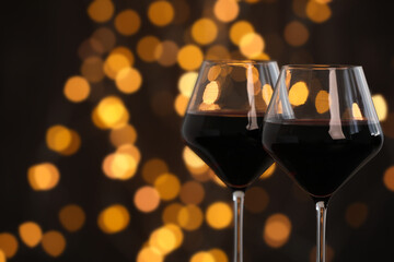 Tasty red wine in glasses against dark background with blurred lights, closeup. Bokeh effect