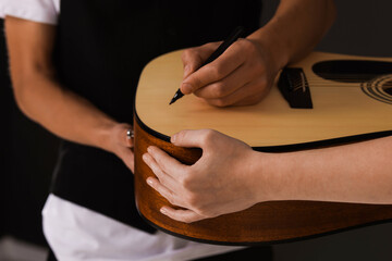 Musician signing autograph on guitar against dark background, closeup