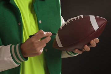 Professional player signing autograph on American football ball black background, closeup