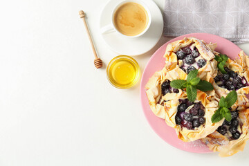 Tasty puff pastries with blueberries, powdered sugar, mint, honey and coffee on white table, flat lay. Space for text