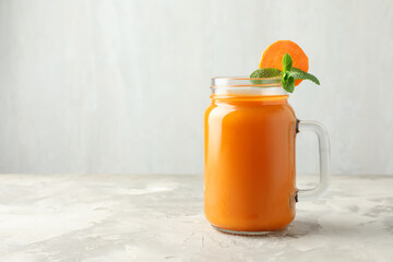 Fresh carrot juice and mint in mason jar on gray textured table, space for text