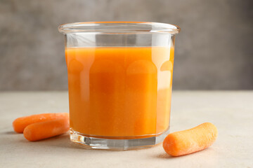 Fresh carrot juice in glass and vegetables on gray textured table, closeup