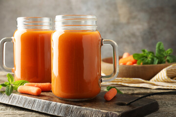Fresh carrot juice in mason jars, vegetables and mint on wooden table against gray background