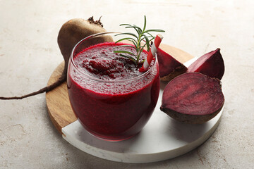 Fresh beetroot smoothie with rosemary in glass and cut vegetable on light textured table, closeup