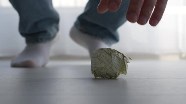 The man bent down to pick up trash from the floor.
A piece of paper on the floor.
A man picks up an object from the floor.
Dirty floor.
The paper ball fell to the floor.
Hand, paper, lift
