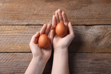 Woman with raw eggs at wooden table, top view