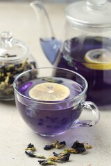 Delicious butterfly pea flower tea with lemon on gray textured table, closeup