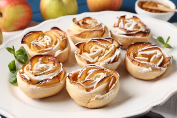 Tasty apple roses with powdered sugar served on table, closeup